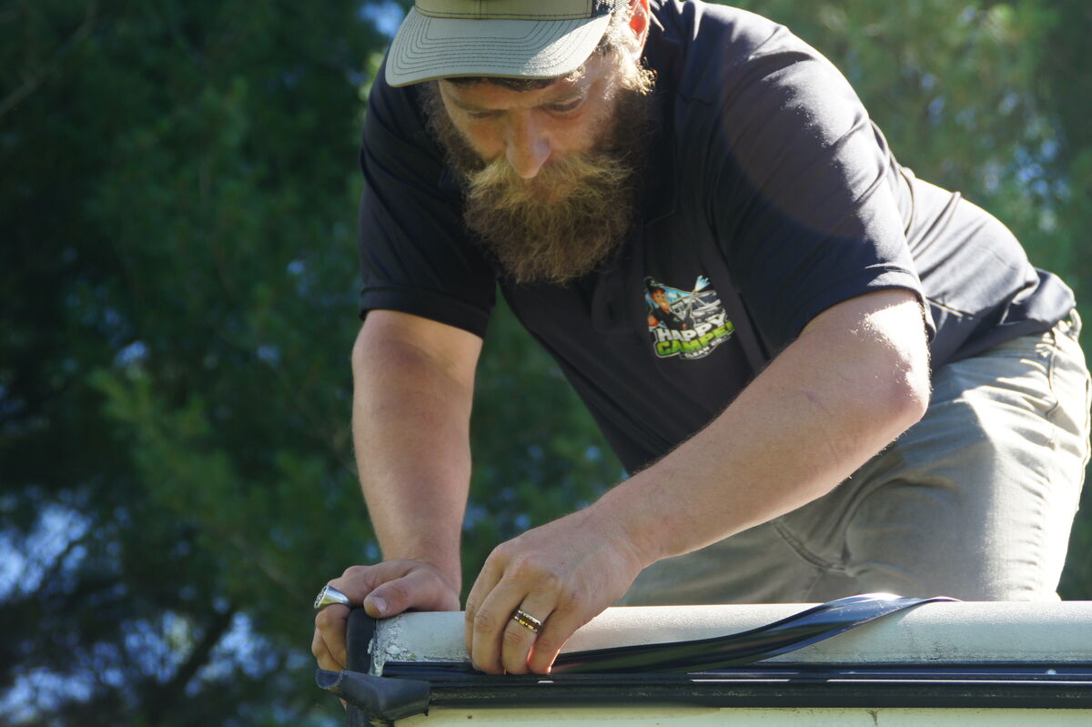 Happy Camper technician closely inspecting an RV roof edge during repair work
