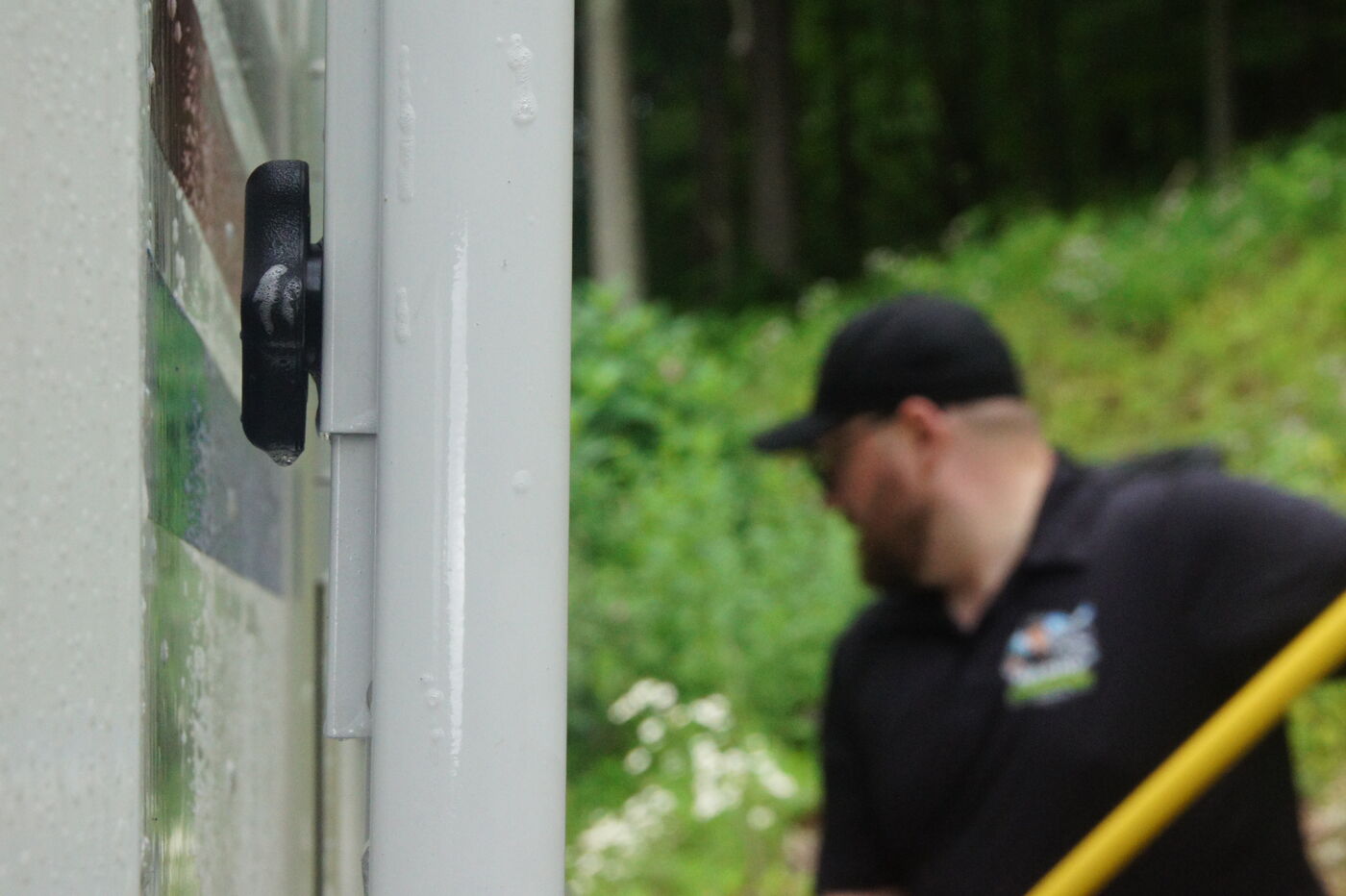 Close up of a wet RV door latch with Happy Camper technician working in the background